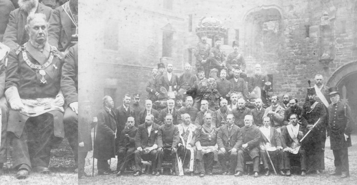 A group photo of 40 men in formal attire the grounds of ruins. A zoomed in image of the man at the centre of the image is on the left of the image.