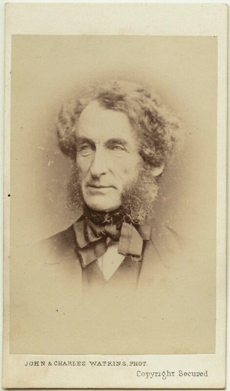 Photograph of a man, showing his head and shoulders. He has dark hair and very bushy sideburns. He is wearing a very elaborately tied bow tie.