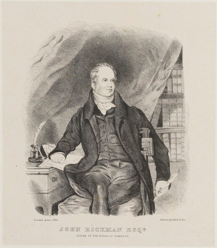 A man in nineteenth-century full suit, sitting with his hand resting on a document on a writing table, with a quill in his hand. In the background to his right is a bookcase, partly covered by a drawn curtain. The caption at the bottom reads John Rickman esq., clerk of the house of commons.