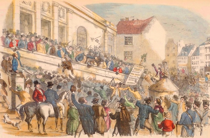 A colour print depicting a public election in Kilkenny. There is a crowded street with hundreds of people, all looking towards another big group of people on the large balcony out the front of an ornate limestone building. The people on the street are looking up gesturing, a few people can be seen fighting. On the balcony people are gesturing to the crowd below, with one man falling off the balcony into the crowd below.