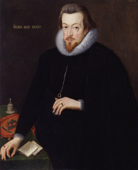 Oil on canvas portrait of a white man's body (not legs) and head. He has brown medium length brown hair and a moustache and trimmed short beard. He is wearing black, and a white neck ruffle. He has a ring on the ring feature of each hand. His right hand is resting on a table covered in a green table cloth, a bell, a red fabric, and a folded up note. To the right of his head are the words 'sero, sed, serio'.